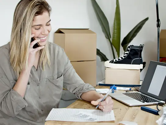 Online store owner taking an order by phone next to a laptop and packed parcels: cover for the post comparing Shopify and WooCommerce in India